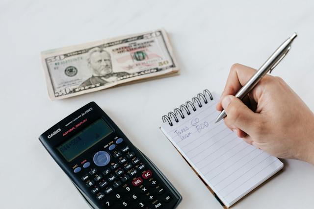 hand-holding-a-pen-and-a-calculator-next-to-a-notepad-and-money