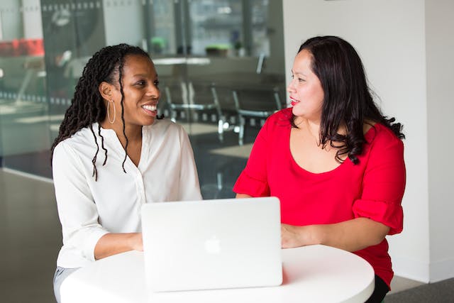 two-people-sitting-at-table-talking-with-laptop-in-front-of-them