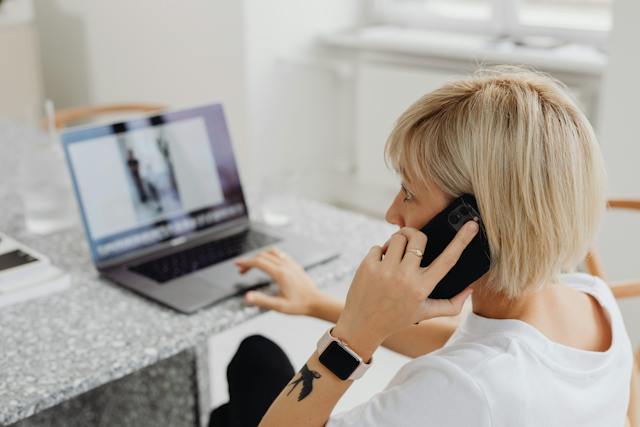 person-sitting-at-a-table-working-on-their-computer-talking-on-the-phone-with-a-property-manager