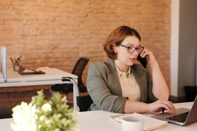 person-sitting-at-desk-talking-on-smartphone-and-working-on-computer