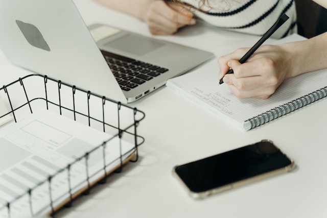 person-writing-notes-on-a-paper-with-their-laptop-open-in-front-of-them