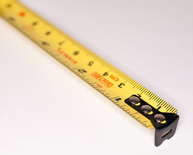 a-close-up-of-a-yellow-measuring-tape-with-black-markings-on-a-white-surface