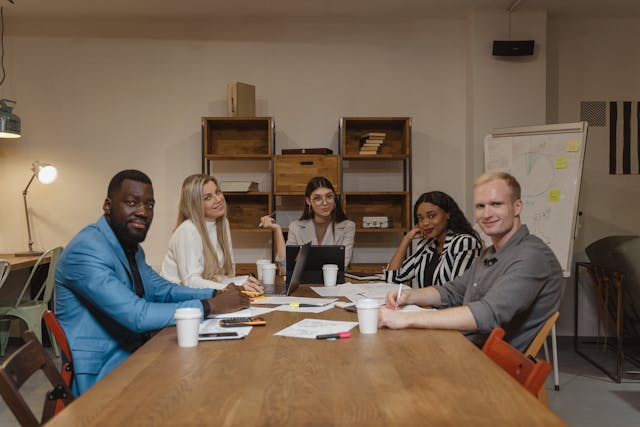 a-diverse-group-of-professionals-sitting-around-a-wooden-table-in-a-modern-office-engaged-in-a-discussion-with-documents-and-coffee-cups