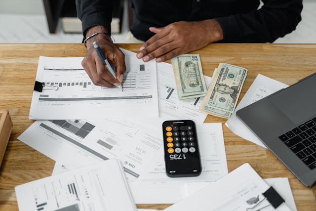 a-person-reviewing-financial-documents-at-a-desk-with-cash-a-calculator-and-a-laptop