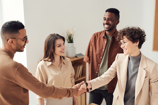 four-professionally-dressed-people-in-a-bright-office-setting-smiling-and-talking-two-of-them-are-shaking-hands-suggesting-a-friendly-business-agreement-or-introduction