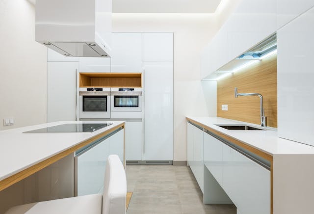 a-bright-modern-kitchen-with-glossy-white-cabinets-built-in-ovens-a-sleek-island-and-wood-accents-along-the-backsplash-and-countertop-edges