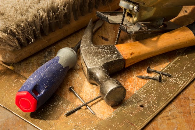 a-close-up-of-woodworking-tools-on-a-dusty-workbench-including-a-hammer-screwdriver-saw-nails-screws-and-a-brush
