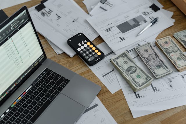 a-cluttered-desk-with-financial-documents-a-laptop-a-smartphone-displaying-a-calculator-app-and-stacks-of-u-s-dollar-bills