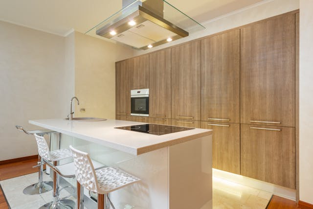 a-contemporary-kitchen-with-a-large-white-island-three-modern-bar-stools-wood-paneled-cabinets-and-built-in-appliances