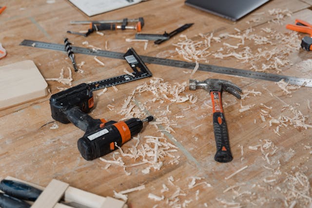 a-messy-workbench-covered-in-wood-shavings-with-various-tools-scattered-around-including-a-power-drill-hammer-clamps-rulers-and-drill-bits