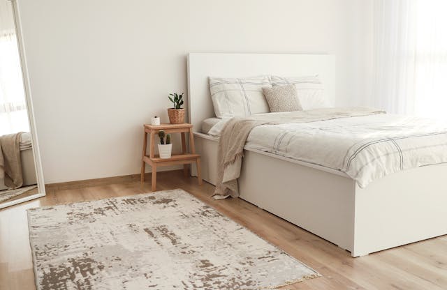 a-minimalistic-bedroom-with-a-white-bed-light-bedding-a-wooden-nightstand-with-potted-plants-a-neutral-toned-rug-and-a-full-length-mirror-against-the-wall