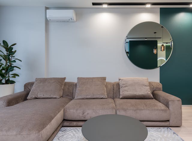 a-modern-living-room-with-a-large-brown-sectional-sofa-a-round-gray-coffee-table-a-circular-wall-mirror-and-a-two-tone-wall-with-white-and-dark-green-accents