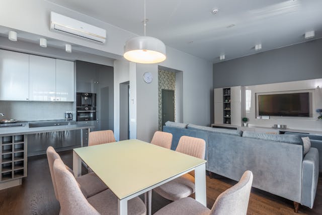 a-modern-open-concept-living-space-with-a-dining-table-and-six-chairs-a-gray-sofa-facing-a-wall-mounted-tv-and-a-sleek-kitchen-with-white-and-gray-cabinets