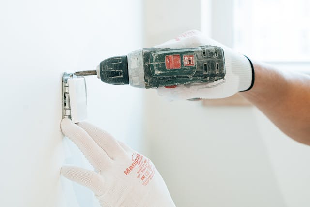 a-person-wearing-white-work-gloves-uses-a-power-drill-to-install-or-adjust-a-wall-outlet