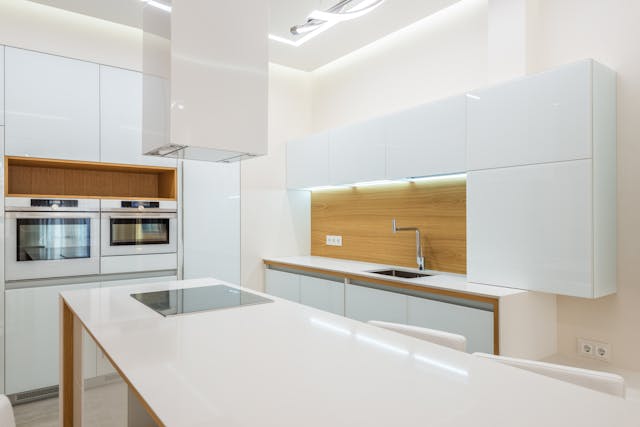 a-sleek-modern-kitchen-with-glossy-white-cabinets-built-in-appliances-a-large-island-with-an-induction-cooktop-and-wood-accents-on-the-backsplash-and-shelving