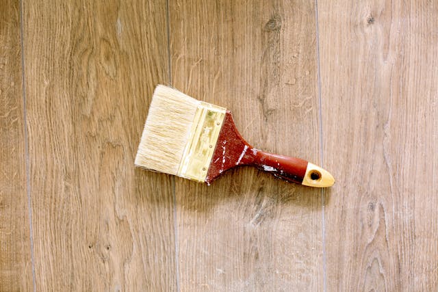 a-wide-paintbrush-with-a-red-and-gold-handle-lying-on-a-wooden-floor