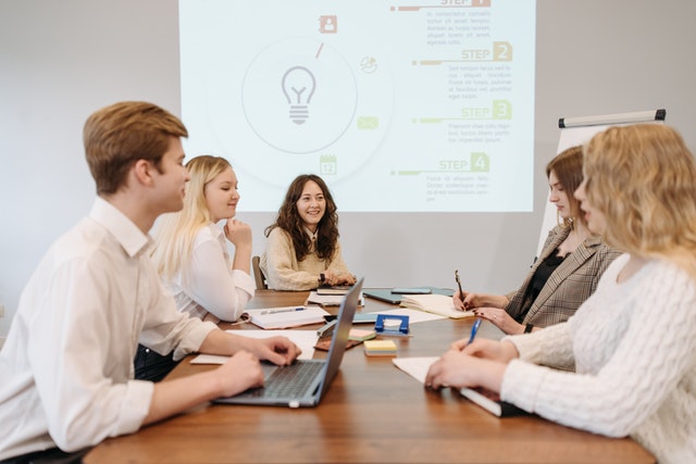 group-of-business-professionals-sitting-at-a-table-discussing-marketing-techniques-using-a-projector-and-computer