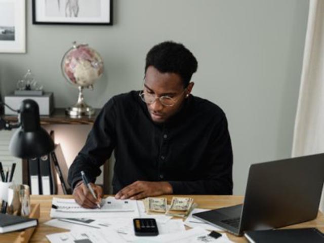 man-sitting-at-a-desk-reviewing-financial-documents-with-a-laptop-calculator-and-stacks-of-cash