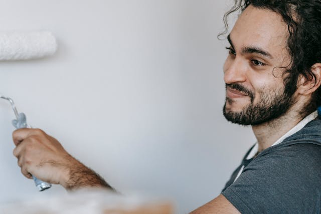 man-smiling-while-using-a-paint-roller-to-apply-white-paint-to-a-wall