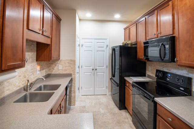 modern-galley-kitchen-with-wooden-cabinets-black-appliances-dual-sinks-and-recessed-lighting