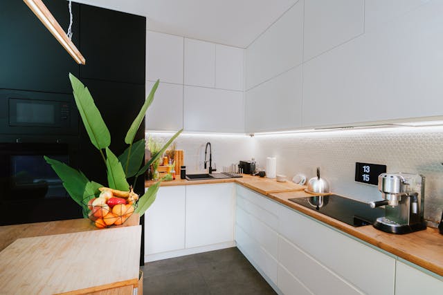 modern-kitchen-with-white-cabinets-wooden-countertops-under-cabinet-lighting-and-a-counter-display-featuring-a-tropical-plant-and-fruit-basket