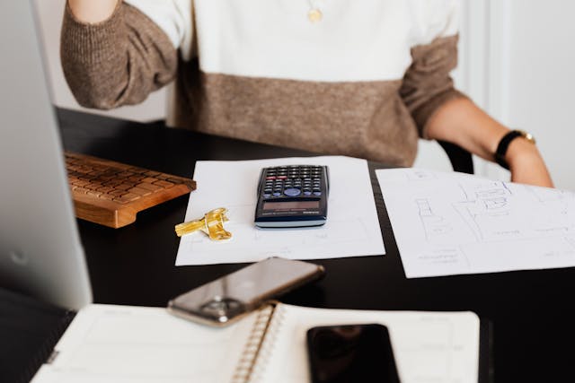 person-sitting-at-a-desk-with-a-scientific-calculator-house-keys-architectural-plans-and-office-supplies-suggesting-financial-planning