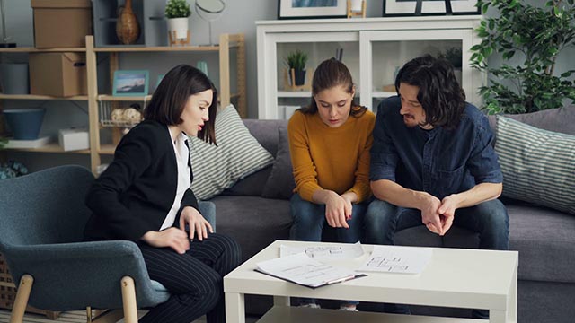 professional-discussing-floor-plans-with-a-couple-seated-in-a-living-room-setting