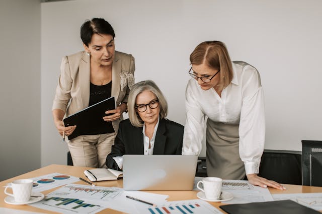 three-professional-women-discussing-data-on-a-laptop-at-a-desk-with-financial-charts-and-documents