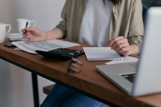 woman-working-at-a-desk-with-financial-documents-a-calculator-notebook-glasses-and-a-laptop