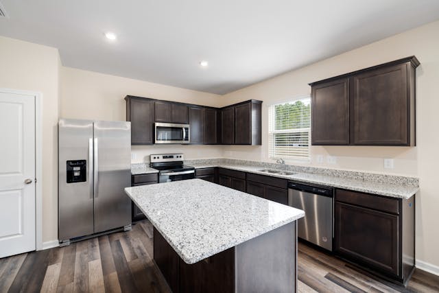 a-beige-kitchen-with-speckled-granite-counters-and-dark-wood-cabinets