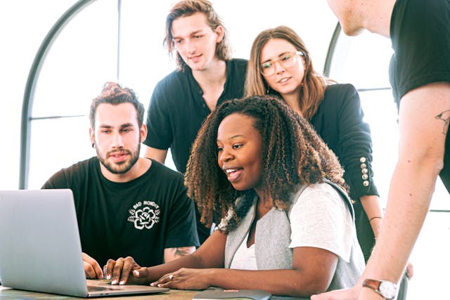 group-of-young-professionals-gathered-around-a-laptop-collaborating-and-smiling