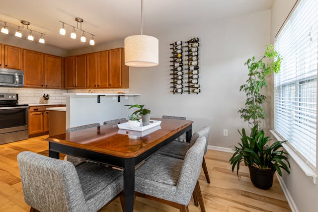 modern-dining-area-with-a-wooden-table-gray-chairs-indoor-plants-and-a-wall-mounted-wine-rack-near-a-bright-kitchen