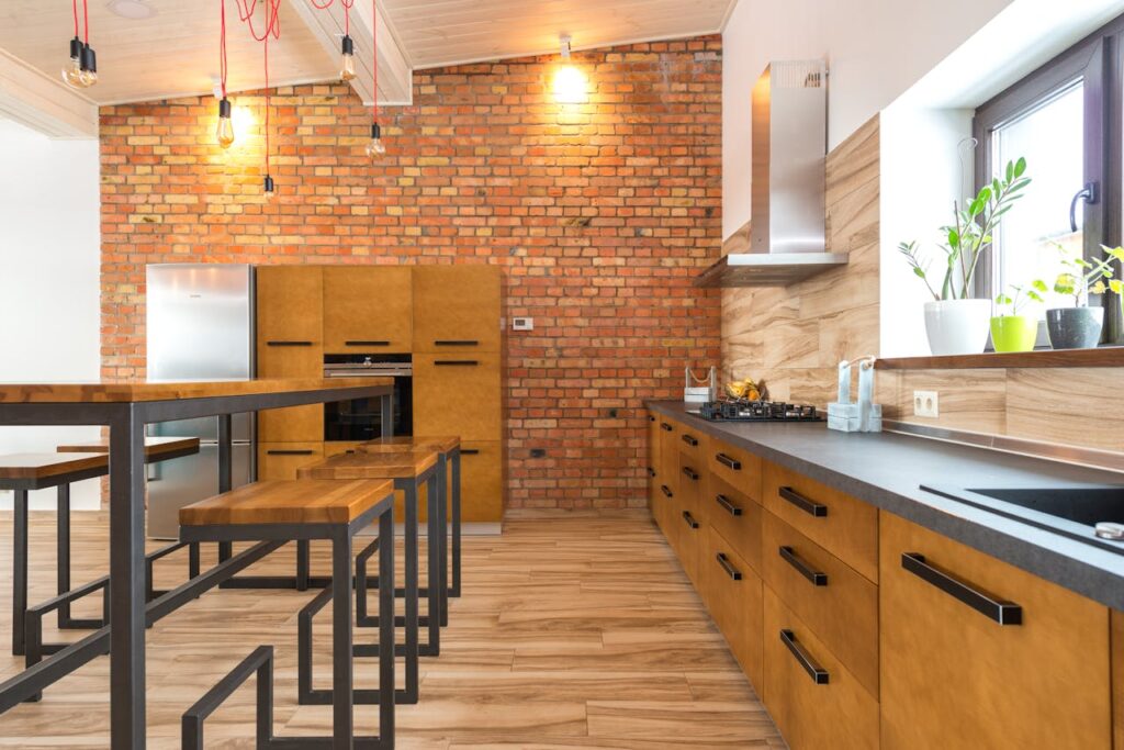 modern-kitchen-with-wood-cabinetry-a-brick-accent-wall-bar-seating-and-potted-plants-by-the-window