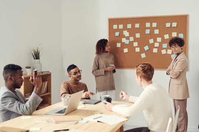 team-meeting-in-a-modern-office-with-people-discussing-ideas-in-front-of-a-corkboard-with-sticky-notes