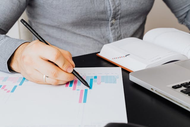 person-analyzing-a-bar-chart-at-a-desk-with-a-laptop-and-notebook