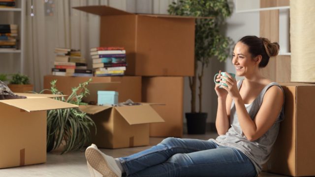 Relaxed-woman-holding-a-cup-of-tea-sitting-on-the-floor-surrounded-by-moving-boxes