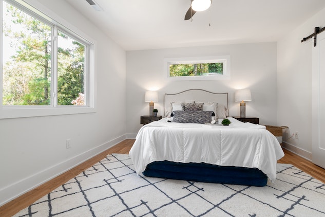 a bedroom with a large window, a queen-sized bed and large black and white area rug