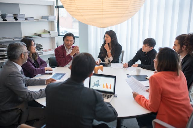 a-diverse-group-of-professionals-having-a-meeting-around-a-conference-table-with-laptops-and-documents