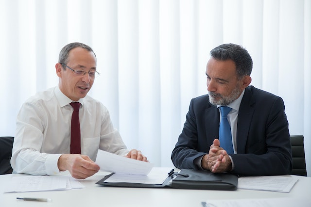 a person with a red tie looking over a report with someone in a blue tie