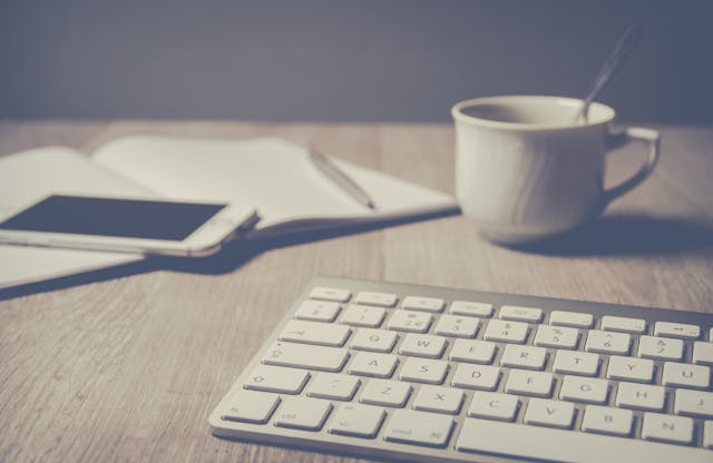 compuer-keyboard-phone-coffee-cup-and-notebook-layed-out-on-a-table