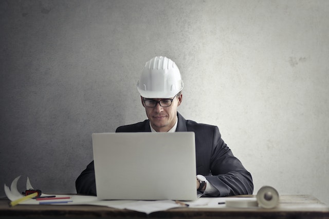 contractor in a white hard hat working on a computer at work station