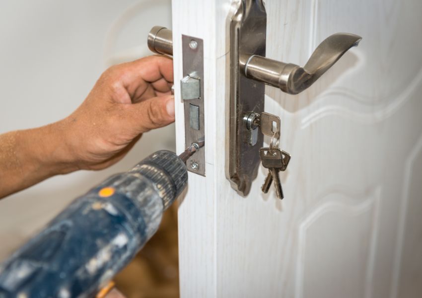contractor using a drill to fix a lock on a door