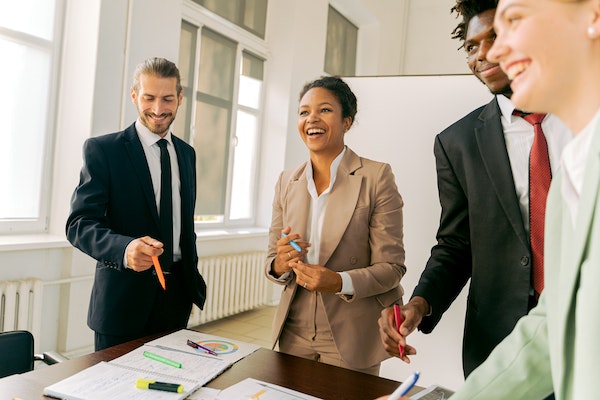 four real estate experts smiling and standing around a conference table looking at documents