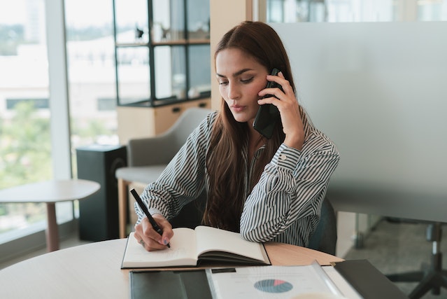 marketing professional talking on the phone and taking hand-written notes