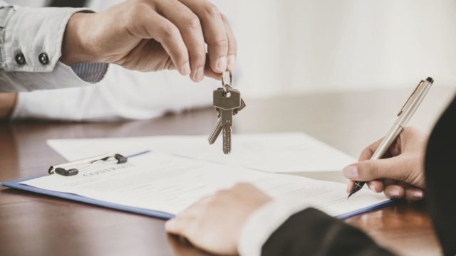 person-dangling-a-key-over-someone-else-who-is-signing-a-document