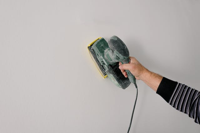 person-holding-electric-sander-to-a-wall