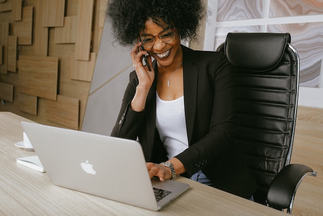 person in a white shirt and black suit jacket talking on the phone and looking at their computer