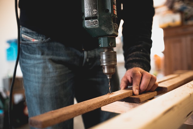 person in blue jeans using a drill on a piece of wood