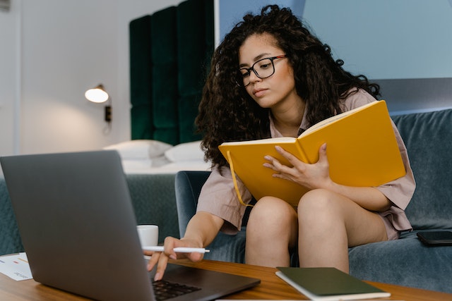 person-sitting-on-a-couch-holding-a-notebook-and-using-their-laptop