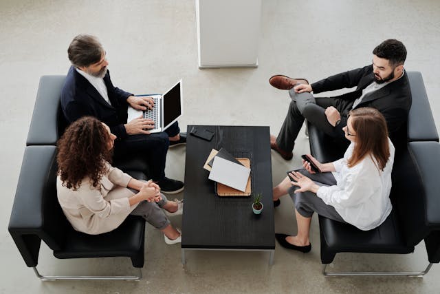 A group of four professionals sitting in a modern office lounge, engaged in a discussion.